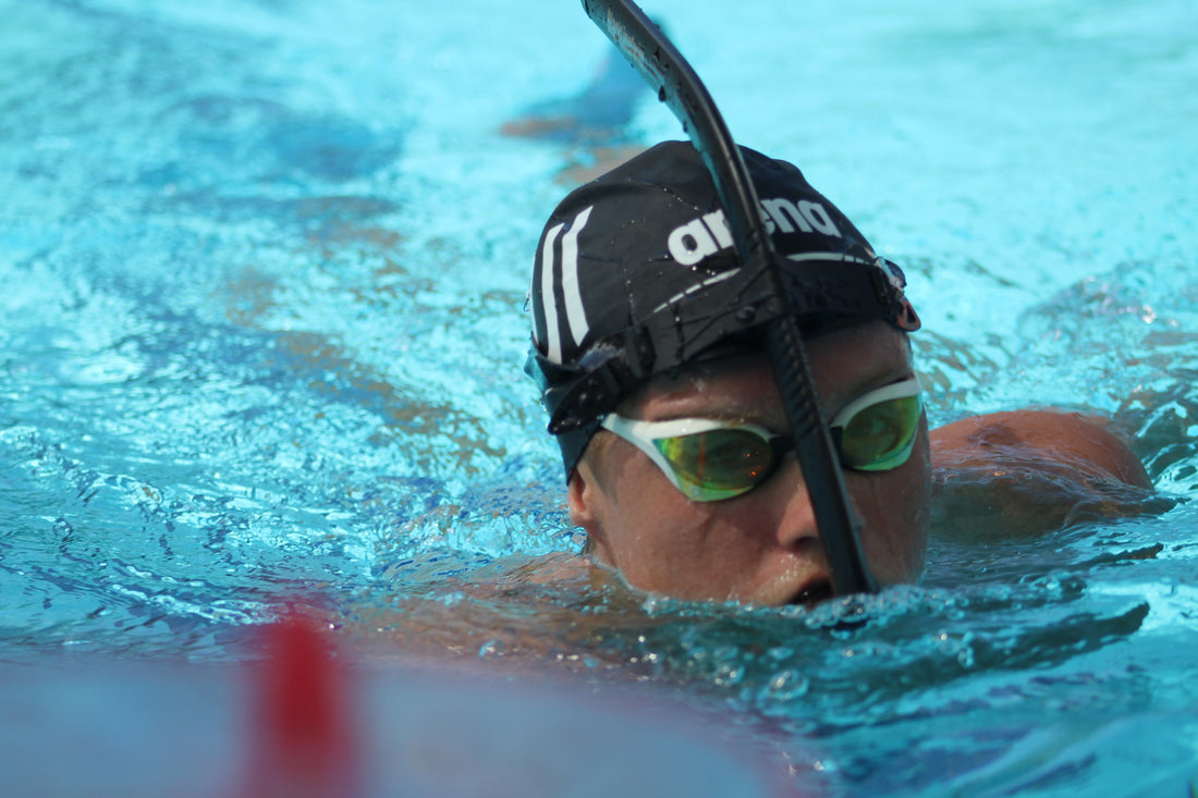 Swimmer training in the pool using swim paddles and a center snorkel to improve stroke technique