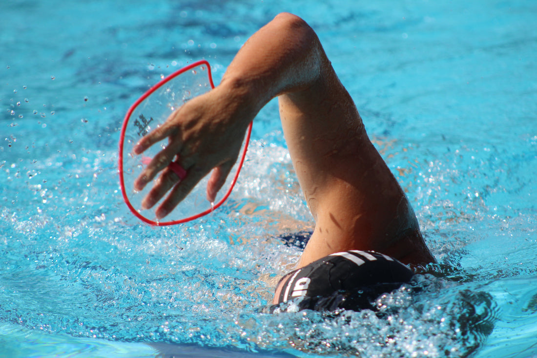 Swimmer wearing hand paddles during a pool session to build better technique and feel for the water.